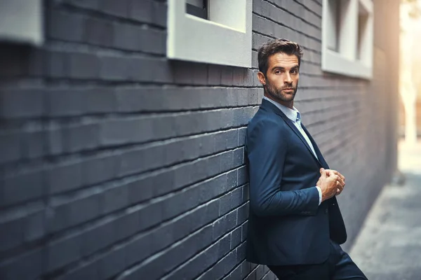 Dressed to impress. a handsome young businessman standing against a grey facebrick wall
