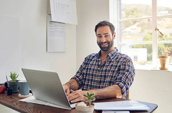 Growing my business day by day. Portrait of a smiling man sitting at a desk working on a laptop