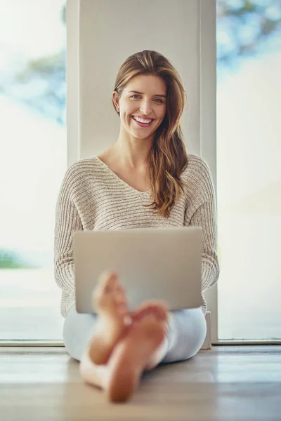 Home is where the wifi is. Portrait of a happy young woman using her laptop while sitting on the floor at home