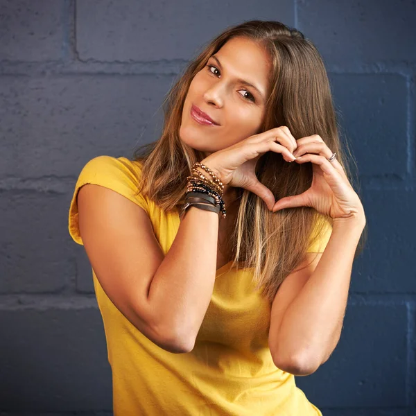 Love from me to you. Portrait of a young woman making a heart gesture with her hands against a brick wall background