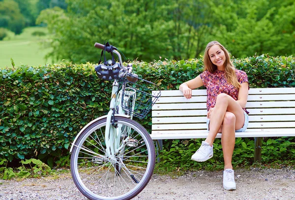 My idea of a great weekend. a young woman sitting on a bench while out for a cycle in the park