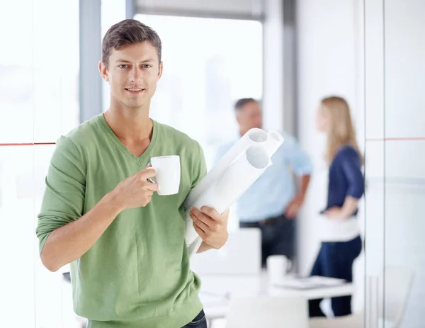 Creative by design. Portrait of a young architect holding a cup of coffee and his blueprints