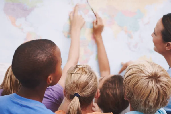 The world is full of oppurtunities. A group of excited schoolchildren pointing at a world map as their teacher looks on