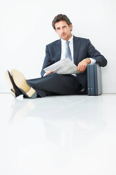 Handsome business man sitting against wall with newspaper. Portrait of handsome business man sitting against wall with newspaper and suitcase