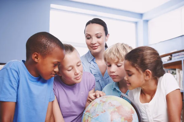 Wow, the world is such a big place. A pretty young geography teacher teaching her students about the world using a globe of earth