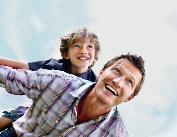 Cheerful mature man with his son on back flying against sky. Portrait of a cheerful mature man with his son on back flying against sky