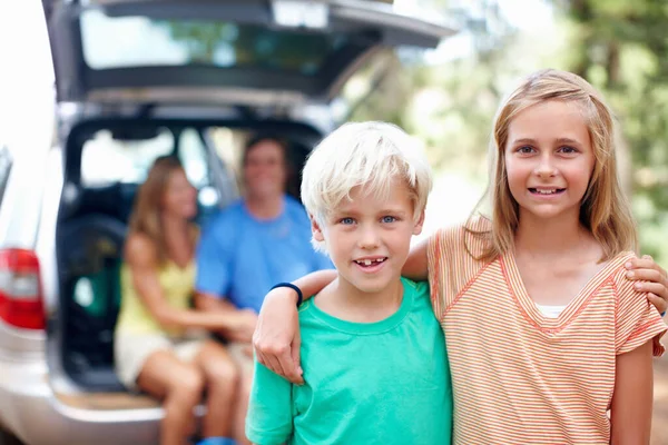 Brother and sister standing with arms around and smiling. Brother and sister standing with arms around and parents sitting in the back of a car