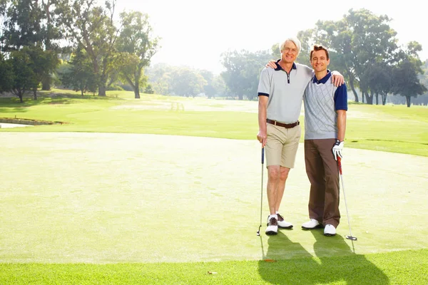 Father and son playing golf. Full length of father and son standing on golf course with arms around