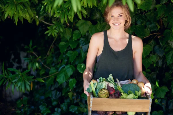Save money the easy way. A young woman holding a crate of vegetables outdoors
