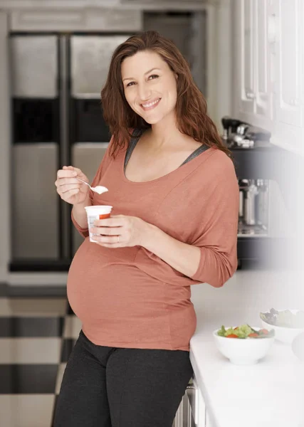 Enjoying a nutritious snack. a young pregnant woman eating a yogurt in the kitchen