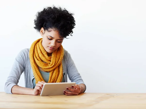Getting lost in the digital world. A pretty young woman sitting at a table and using a tablet against a white background