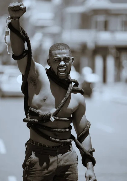 Protest, fist and man in rope and handcuffs in city protesting against discrimination, oppression or slavery and racism. Black lives matter, justice and angry male in street fighting for human rights.