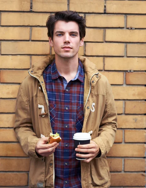 Food for his mind, body and soul. a young man standing outdoors with a half eaten burger and take away coffee