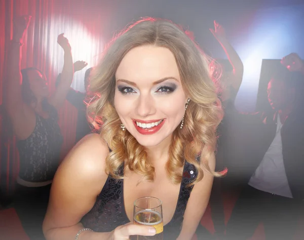 Dancing the night away. A lovely young blonde woman smiling at the camera while standing on the dancefloor holding a glass of wine