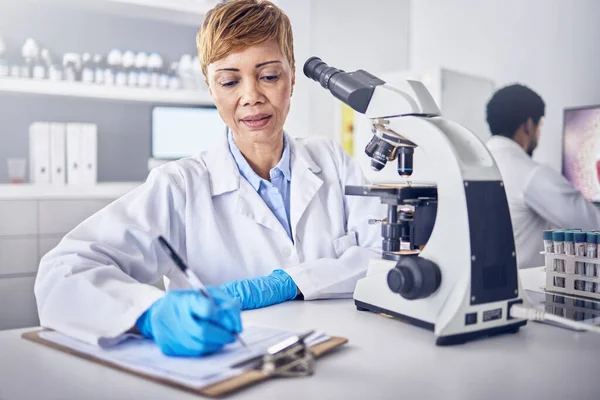 Senior black woman, research or scientist writing a science report in a laboratory for medical data analysis. Healthcare, focus or doctor working on chemistry paperwork, documents or development.