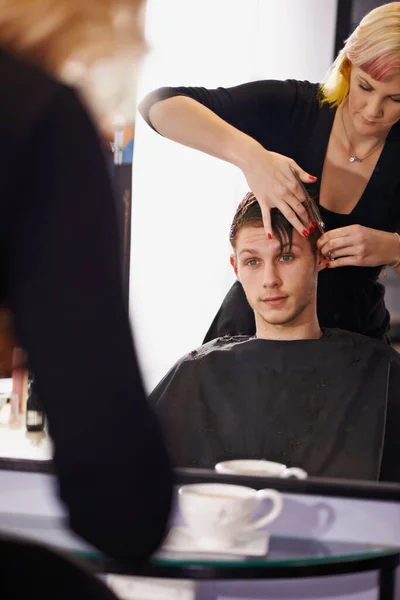 Cant wait to see the end result. A young man having his hair styled by a hairdresser