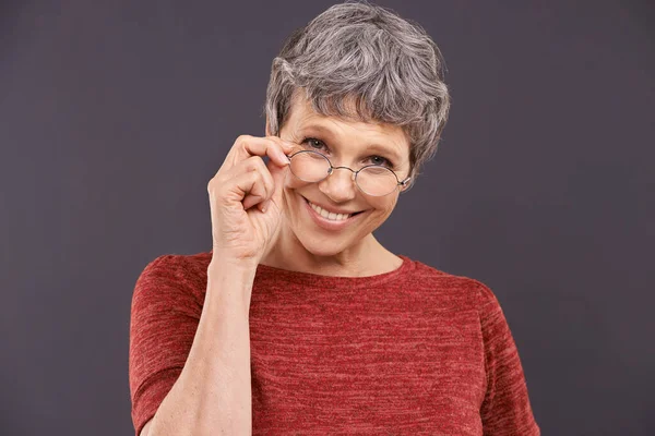 Seeing things clearly. Studio portrait of a happy elderly woman wearing glasses against a gray background