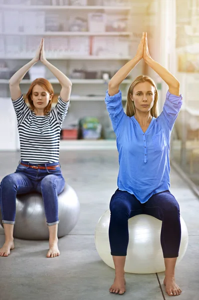 Yoga in the office. Full length shot of two businesswomen doing yoga in the office