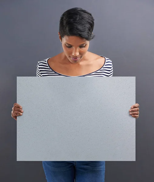 Reading your copy. Studio shot of a beautiful young woman holding a blank placard against a grey background