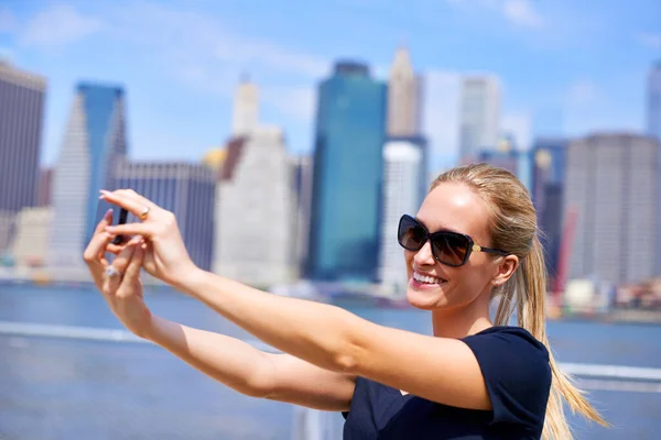 Enjoying the city sights. an attractive young woman taking a photo while standing beside a river in a city