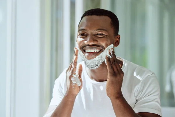 Shaving, cream and black man grooming face for clean look, hygiene care and beauty morning routine in the bathroom. Skincare, happy and African person ready to shave beard and facial hair with foam.