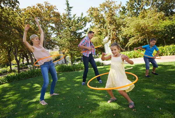 A family that plays together stays together. A happy family hula hooping in the park on a sunny day