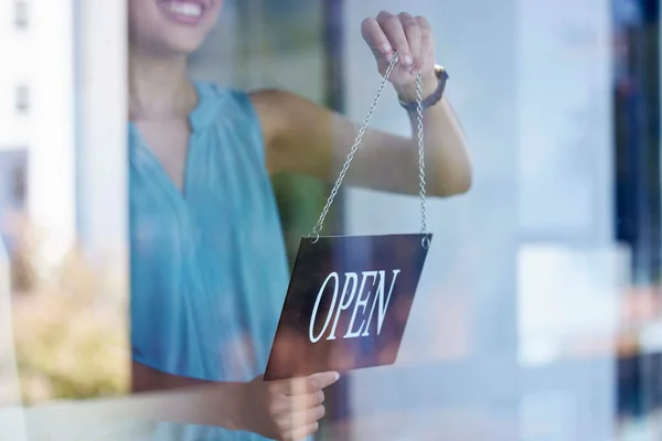 Small business, woman and entrepreneur with open sign excited at professional shop window entrance. Smile of proud and happy business owner holding sign for store opening with enthusiasm