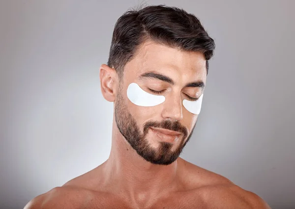Skincare, beauty and man with mask for eyes on gray background for wellness, facial treatment and dermatology. Grooming, luxury spa and male with face patch, eye pads and cosmetics products in studio.