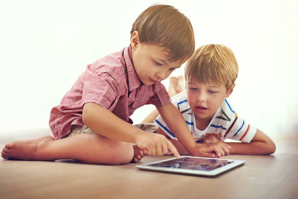 Theres so much for them to learn online. two little boys using a digital tablet together while sitting on the floor