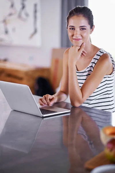 Keeping connected at home. an attractive young woman using her laptop in the kitchen