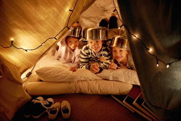 What imaginations. three cute little children with pot helmets in a blanket fort