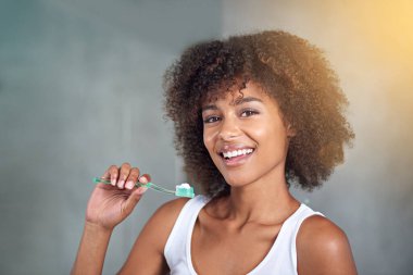 I brush three times per day. Cropped portrait of a young woman brushing her teeth in the bathroom clipart