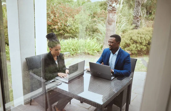 Business people, man and black woman in meeting on terrace, laptop and finance goal on business trip. Black man, woman and teamwork in morning business meeting on patio, hotel or garden for planning.