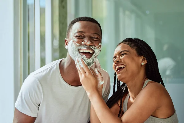 Skincare wellness, happy couple in bathroom and shaving face with product for facial treatment. Laughing together in home, natural beauty and funny girlfriend helping black man with cream application.