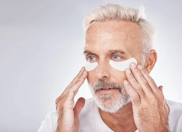 Skincare, eyes patch and man in studio for dermatology facial, face cosmetics or collagen mask advertising or marketing mockup. Senior model, hands application and eye patches or anti aging product.