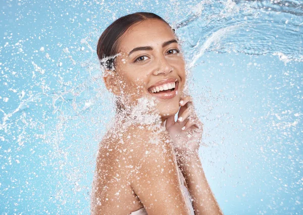 Happy woman, face or water splash skincare on blue background studio for dermatology healthcare wellness, hygiene maintenance or grooming. Portrait, smile or beauty model with water drops in cleaning.