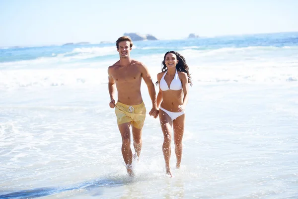 Enjoying the sunshine. A happy couple in swim wear running on the beach together