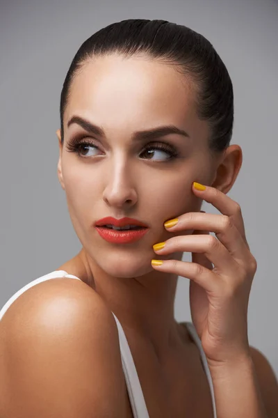 Showing off a trendy manicure. An attractive young woman wearing red lipstick and colourful nail polish
