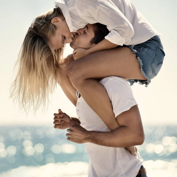 我们在一起很快乐一个女人坐在男朋友的肩上 在海滩上给他一个吻 — 图库照片