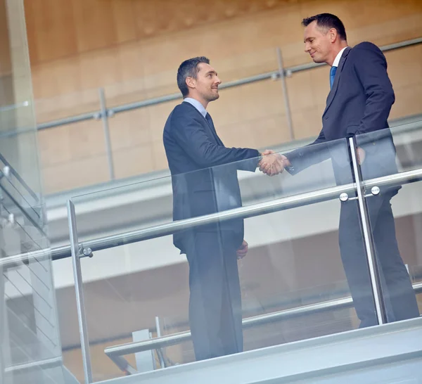 Low angle, business people and corporate handshake in modern office, finance company and investment deal startup. Men, shaking hands and partnership gesture for insurance workers in welcome greeting.