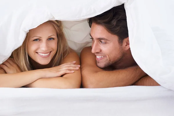 Couple under cover. A couple lying on a bed under the duvet covers and smiling