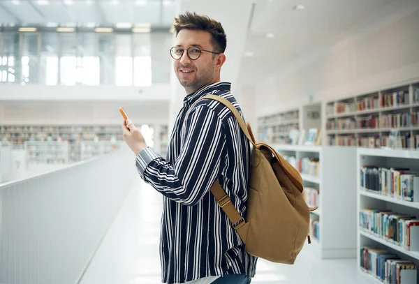Student man, library portrait and phone, smile and chat on social media for communication. College student, smartphone and app for university email in education, learning and studying for future goal.