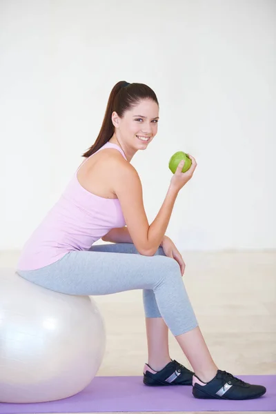 Workout snack. Portrait of a young woman sitting on an exercise ball and eating an apple