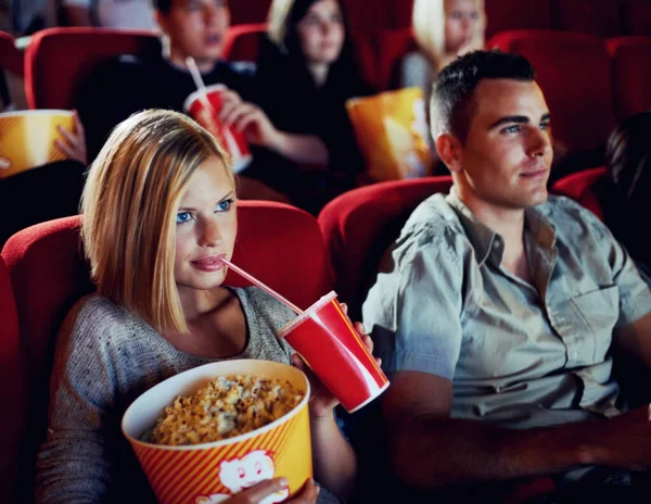 Lose yourself in an imaginary world. A beautiful young woman drinking a soft drink and eating popcorn in a movie