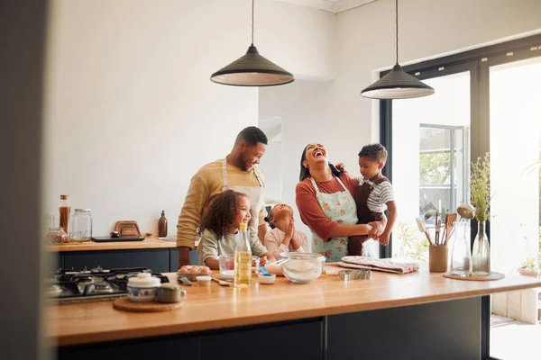 A happy mixed race family of five relaxing in the kitchen and cooking together. Loving black family being playful while baking together. Young couple bonding with their foster kids at home.