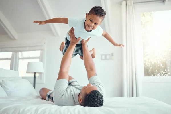 Cute little mixed race boy lying in fathers arms while looking at the camera and smiling. Loving family with father lifting happy little child son playing plane and having fun on bed.