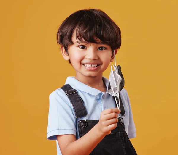 Portrait of an adorable little Asian boy happy while wearing a mask against an orange studio copyspace background. Smiling kid removing his mask.
