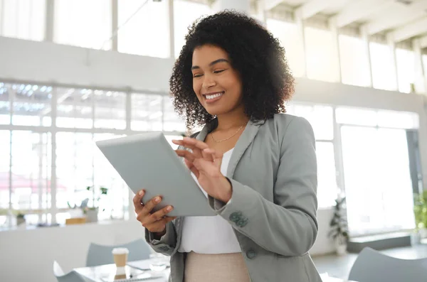 Young happy mixed race businesswoman working on a digital tablet in an office. One cheerful hispanic female boss with a curly afro holding and using social media on a digital tablet at work.