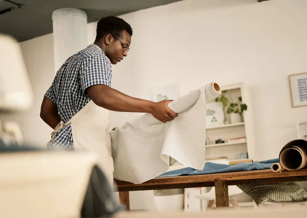 Fashion designer carrying a roll of fabric. African American tailor holding a roll of material. Creative entrepreneur working in his fashion studio. Focused seamstress carrying fabric.