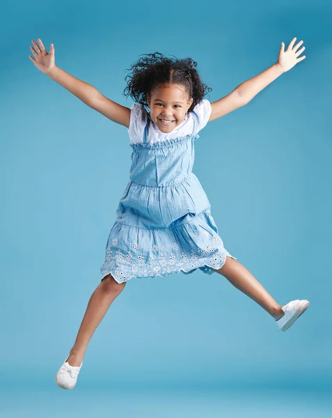 Happy young adorable little hispanic girl jumping in the air, isolated on blue background. Funny preschooler kid expressing her excitement and having fun.